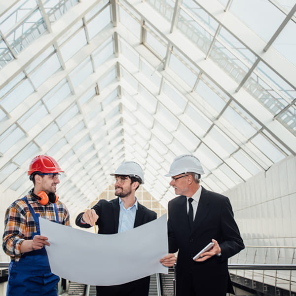 Équipe de professionnels examinant des plans dans un bâtiment industriel à structure métallique