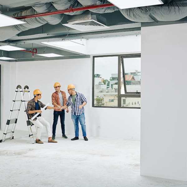 Trois professionnels en casques de chantier discutant des plans de rénovation d'un espace commercial à Montréal