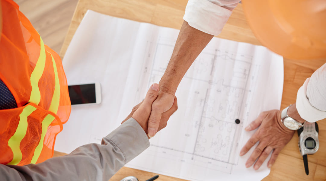 Poignée de main entre un entrepreneur et un client sur des plans de construction commerciale au Québec